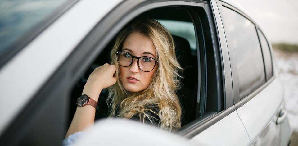 женщина в очках сидит в машине и смотрит через открытое окно водительской двери
